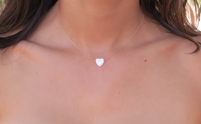 May include: A delicate gold chain necklace with a white heart pendant.