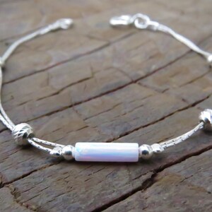 May include: A silver bracelet with a double chain design and iridescent white beads. The bracelet has a clasp closure.