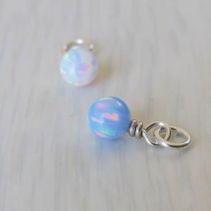 Puede incluir: Dos cuentas de ópalo, una blanca y otra azul claro, con anillas de salto de plata. Las cuentas son iridiscentes y tienen un acabado nacarado.