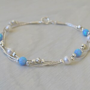 K&ouml;nnte beinhalten: Ein silbernes Armband mit drei Kettenstr&auml;ngen und blauen Opal- und wei&szlig;en Perlen.