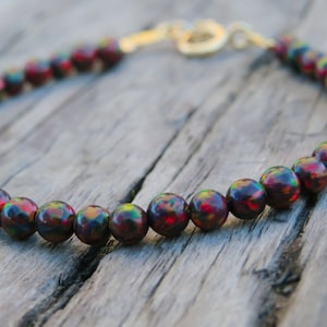 Peut inclure: Un bracelet composé de perles d'opale rouge foncé, vertes et noires avec un fermoir en or.