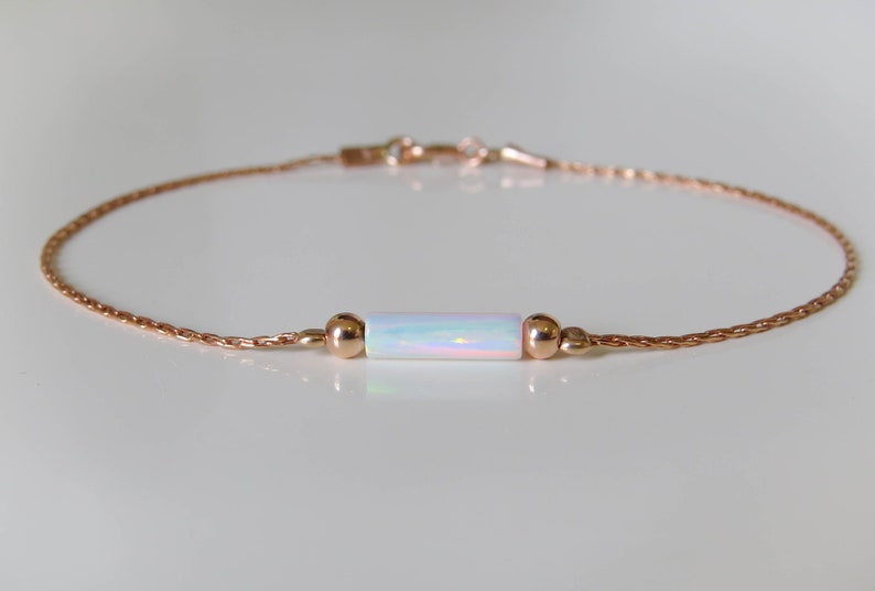 May include: A delicate rose gold chain bracelet with a white opal bar charm. The bracelet is simple and elegant, perfect for everyday wear.