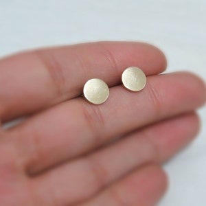 Op de afbeelding: Een paar kleine, ronde, gouden oorbellen. De oorbellen zijn glad en hebben een matte afwerking.