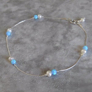 Pu&ograve; includere: Un braccialetto per caviglia in argento con perline di opale blu e perle bianche alternate.