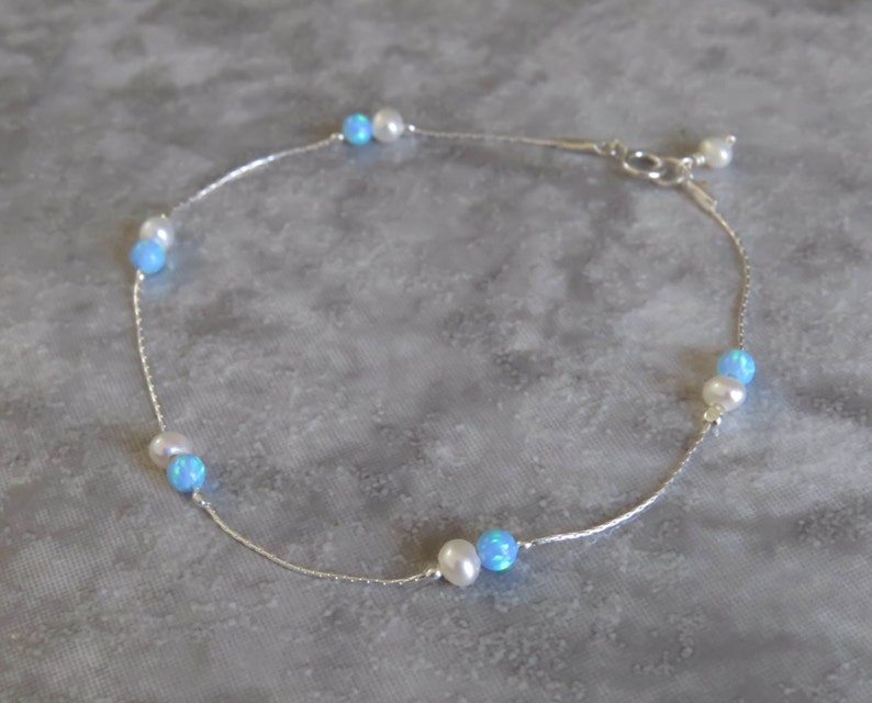 Pu&ograve; includere: Un braccialetto per caviglia in argento con perline di opale blu e perle bianche alternate.