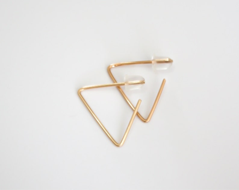 May include: A pair of gold triangle hoop earrings with clear push-back closures.