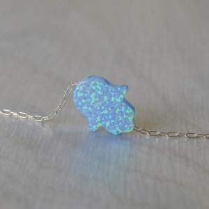 May include: A silver chain necklace with a light blue opal hamsa hand charm.
