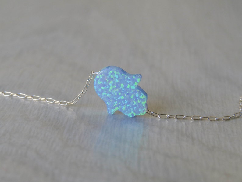May include: A silver chain necklace with a light blue opal hamsa hand charm.