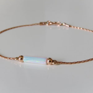 May include: A delicate rose gold chain bracelet with a white opal bar charm. The chain is a braided design and the charm is set between two small rose gold beads.