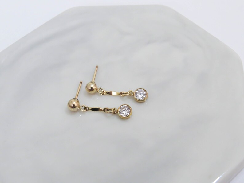 May include: A pair of gold earrings with a small round clear stone dangling from each earring.