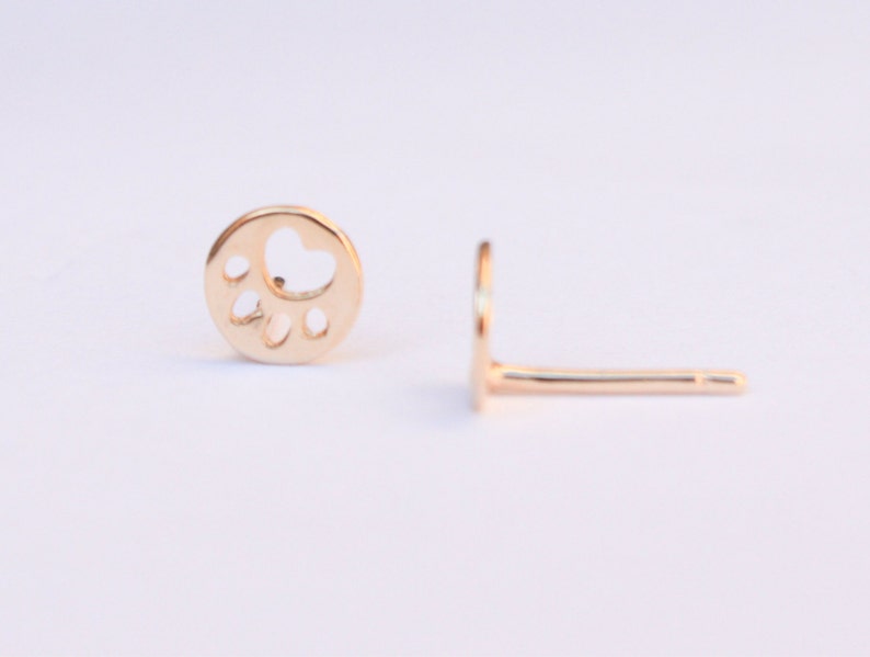 K&ouml;nnte beinhalten: Ein Paar goldfarbene Ohrstecker mit einem Pfotenabdruck-Design. Die Ohrringe sind klein und zart, perfekt f&uuml;r den t&auml;glichen Gebrauch.