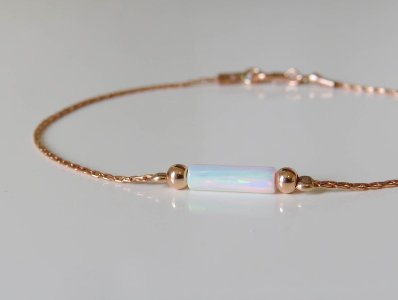 May include: A delicate rose gold chain bracelet with a single white opal bar charm.