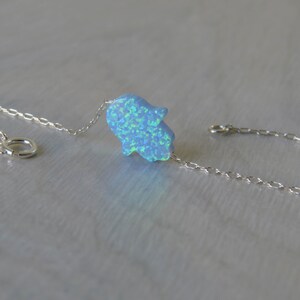 May include: A silver chain bracelet featuring a blue opal hamsa hand charm. The hamsa hand is a symbol of protection and good luck.