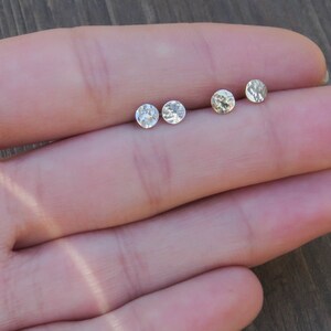 Op de afbeelding: Drie zilveren oorbel studs met een gehamerde textuur. De oorbellen zijn in een rij op een hand gerangschikt.