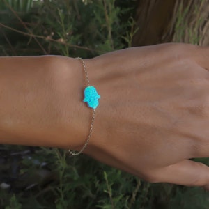 May include: A silver chain bracelet with a blue opal hamsa hand charm.