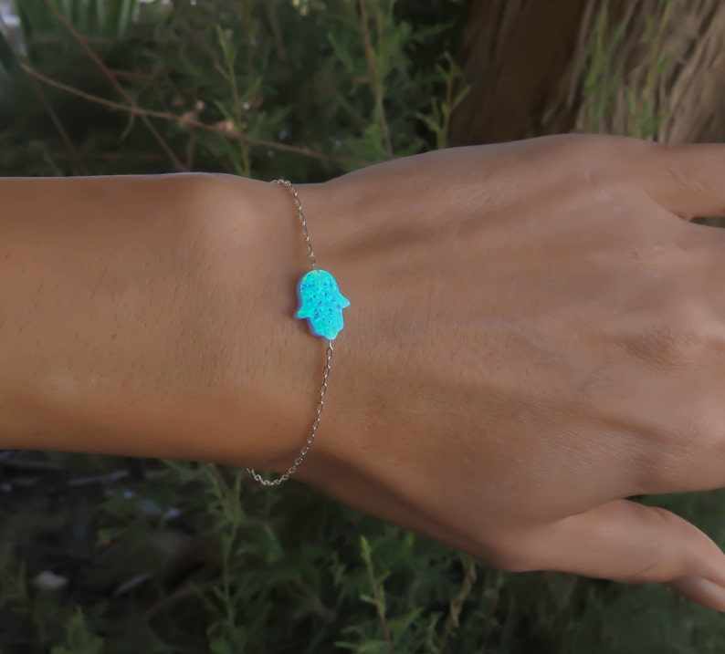 May include: A silver chain bracelet with a blue opal hamsa hand charm.