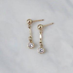 May include: A pair of gold dangle earrings with a small clear stone at the end of each earring.