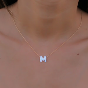 May include: A gold chain necklace with a white letter M pendant.