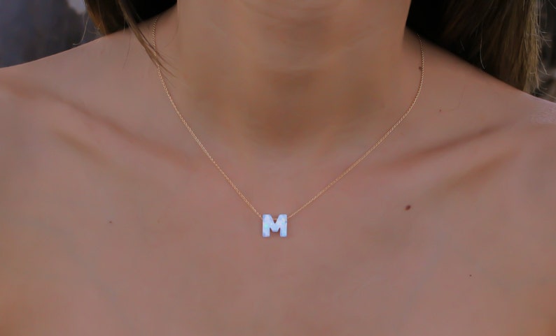 May include: A gold chain necklace with a white letter M pendant.
