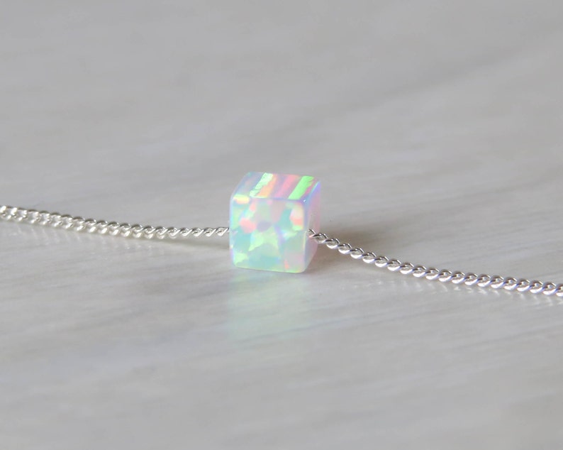 May include: A silver chain necklace with a single iridescent cube-shaped opal pendant.