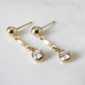 May include: A pair of gold dangle earrings with a small round clear stone at the bottom of each earring.