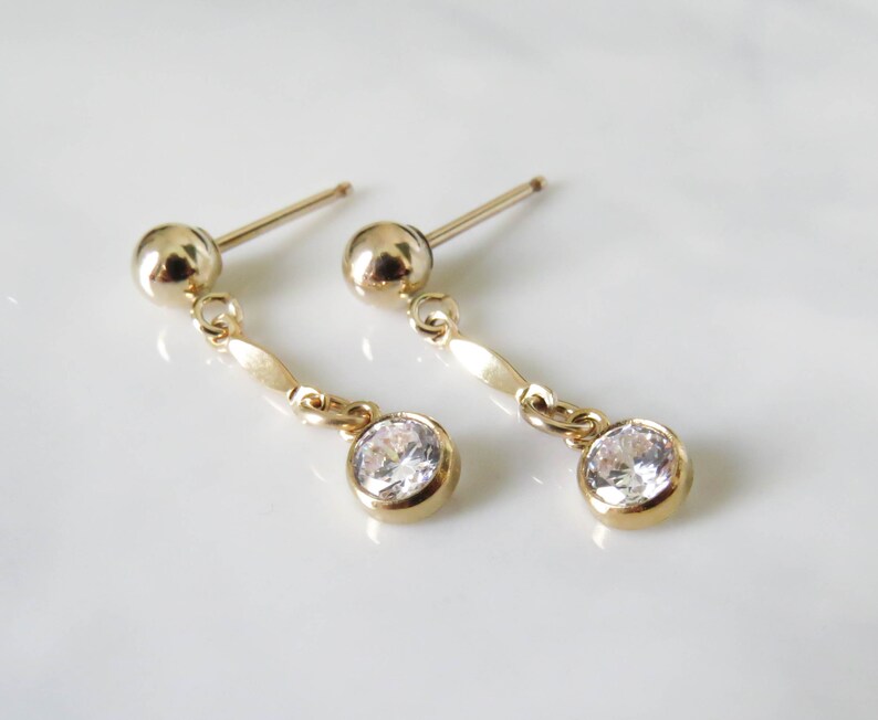 May include: A pair of gold dangle earrings with a small round clear stone at the bottom of each earring.
