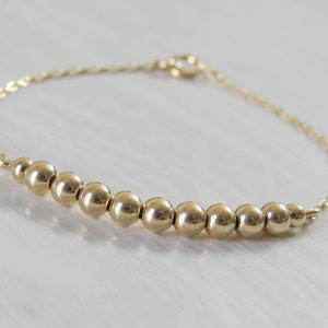 May include: A gold chain bracelet with a row of gold beads.