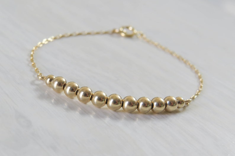 May include: A gold chain bracelet with a row of gold beads.