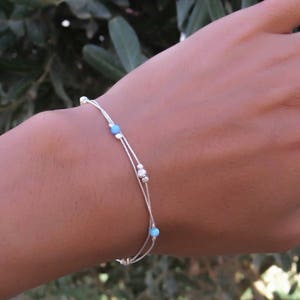 Puede incluir: Una pulsera de plata con tres hebras y pequeñas cuentas azules.