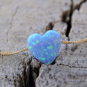 May include: A delicate gold chain necklace with a light blue heart-shaped opal pendant.