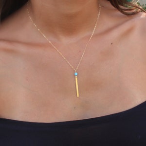 May include: A gold chain necklace with a turquoise gemstone and a long, thin gold bar pendant.