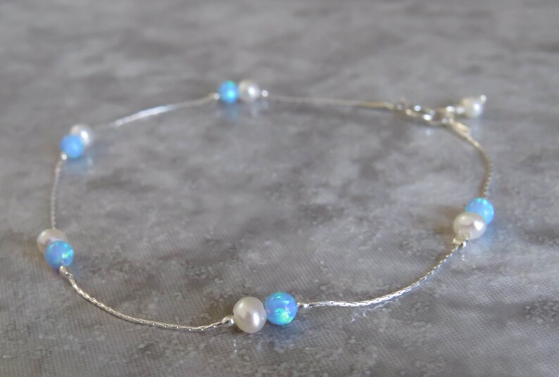 Pu&ograve; includere: Un braccialetto per caviglia in catena d'argento con perle bianche e perle di opale blu alternate.