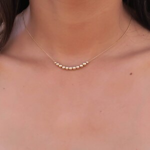 May include: A gold necklace with a curved row of small, round beads.