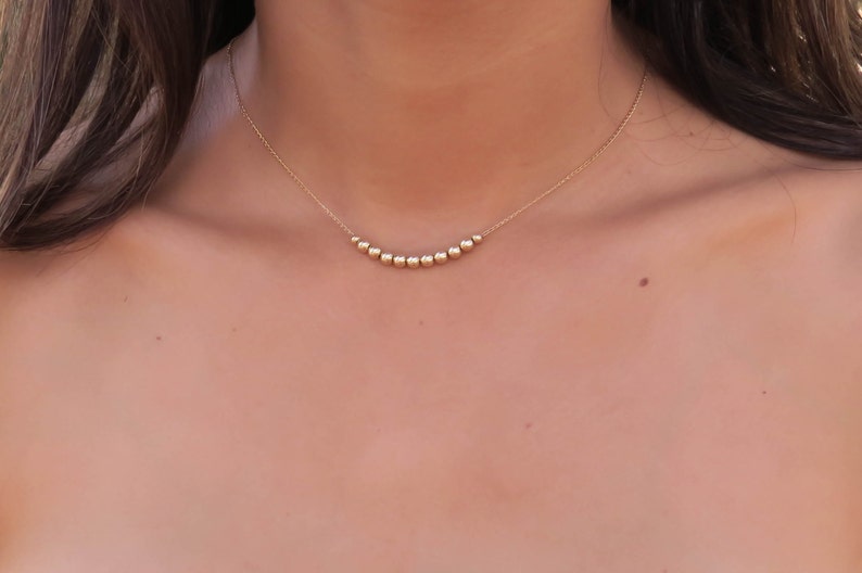 May include: A gold necklace with a curved row of small, round beads.