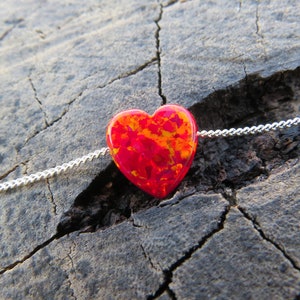 May include: A silver chain necklace with a red and orange heart-shaped opal pendant.