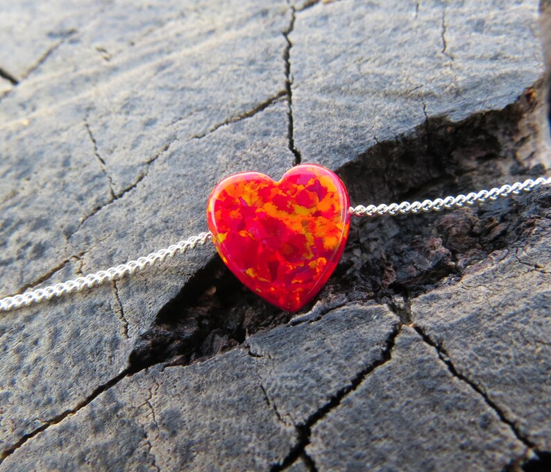May include: A silver chain necklace with a red and orange heart-shaped opal pendant.