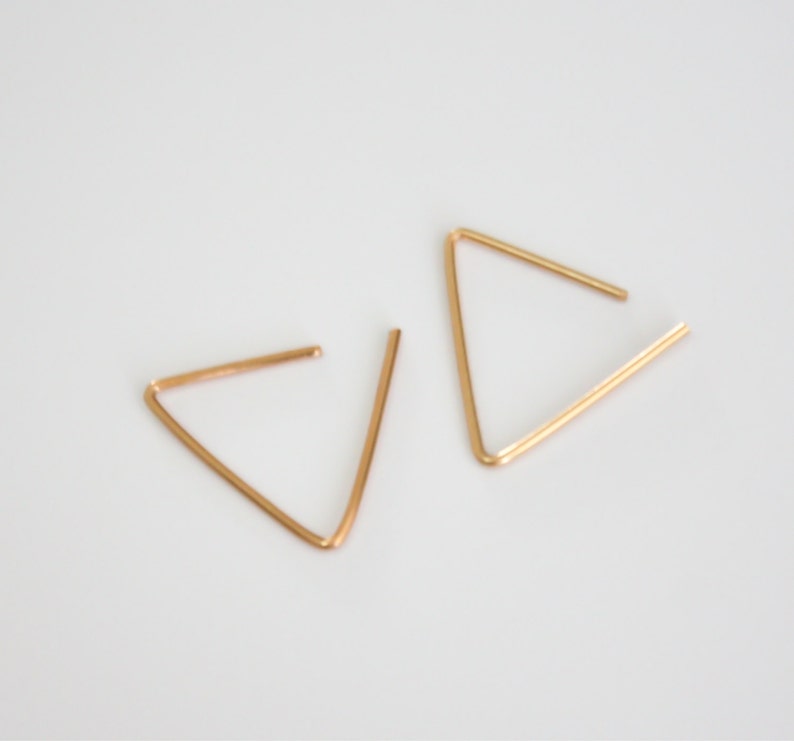 May include: A pair of gold triangle earrings. The earrings are made of thin wire and are simple in design.