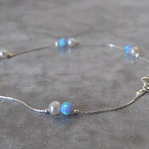 Pu&ograve; includere: Un braccialetto per caviglia in catena d'argento con perline di opale blu e perle bianche alternate.