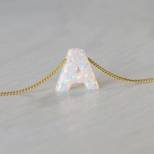 May include: A white opal letter A pendant necklace on a gold chain.