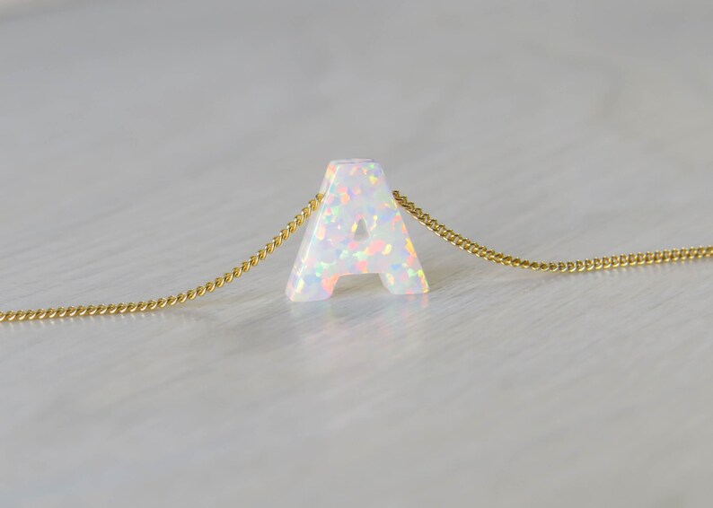 May include: A white opal letter A pendant necklace on a gold chain.