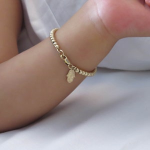 Peut inclure: Un bracelet en or avec un charme hamsa. Le bracelet est composé de petites perles dorées et a une chaîne délicate.