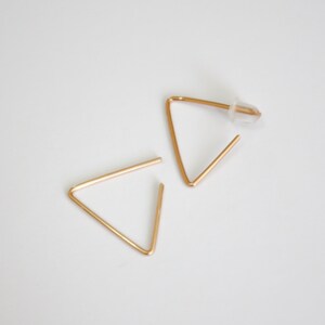 May include: A pair of gold triangle earrings. The earrings are simple and minimalist in design.