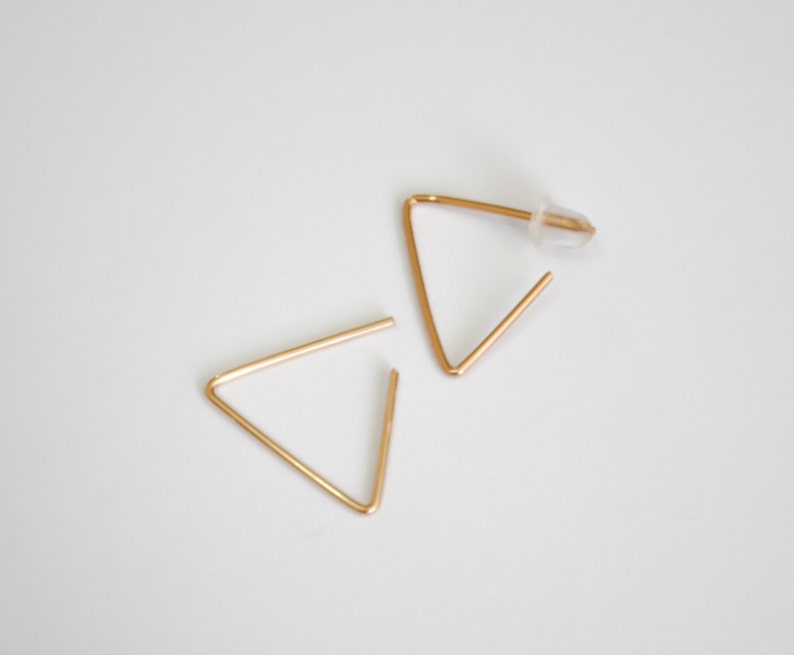 May include: A pair of gold triangle earrings. The earrings are simple and minimalist in design.