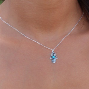 Könnte beinhalten: Eine silberne Kettenkette mit einem Hamsa-Hand-Anhänger mit einem türkisfarbenen Stein in der Mitte.