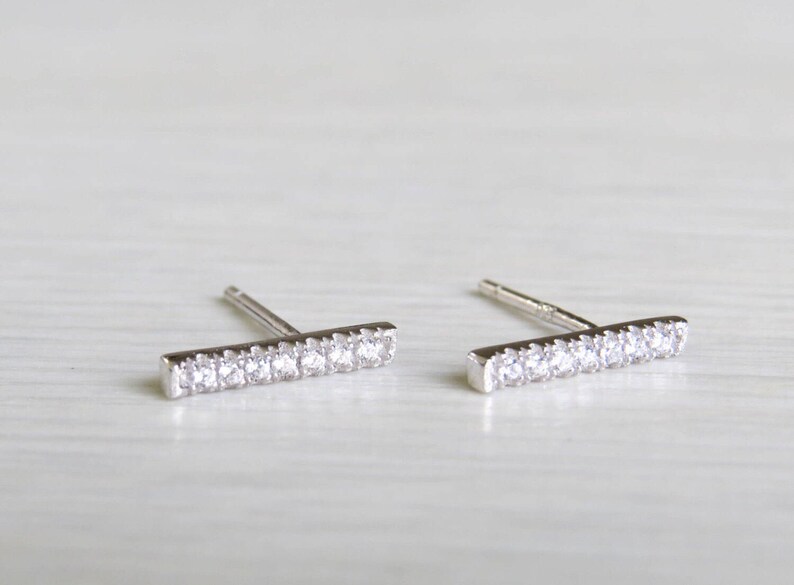 May include: A pair of silver bar stud earrings with clear cubic zirconia stones.