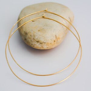 K&ouml;nnte beinhalten: Ein Paar goldene Creolen mit einem schlichten, minimalistischen Design. Die Ohrringe bestehen aus d&uuml;nnem, rundem Draht und sind &uuml;bereinander gestapelt.