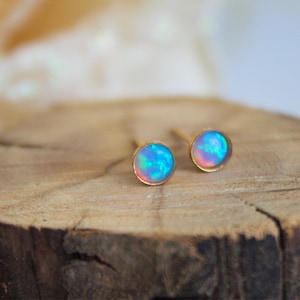 Puede incluir: Un par de pendientes de bot&oacute;n de oro con piedras de &oacute;palo iridiscente. Las piedras tienen un color azul, rosa y blanco.