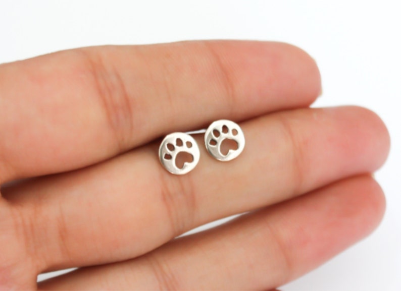 K&ouml;nnte beinhalten: Ein Paar silberne Ohrstecker mit Pfotenabdruck-Design.