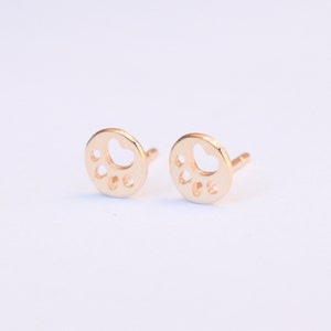 K&ouml;nnte beinhalten: Ein Paar goldfarbene Ohrstecker mit einem Pfotenabdruck-Design. Die Ohrringe sind klein und zart und w&auml;ren ein tolles Geschenk f&uuml;r einen Hundeliebhaber.