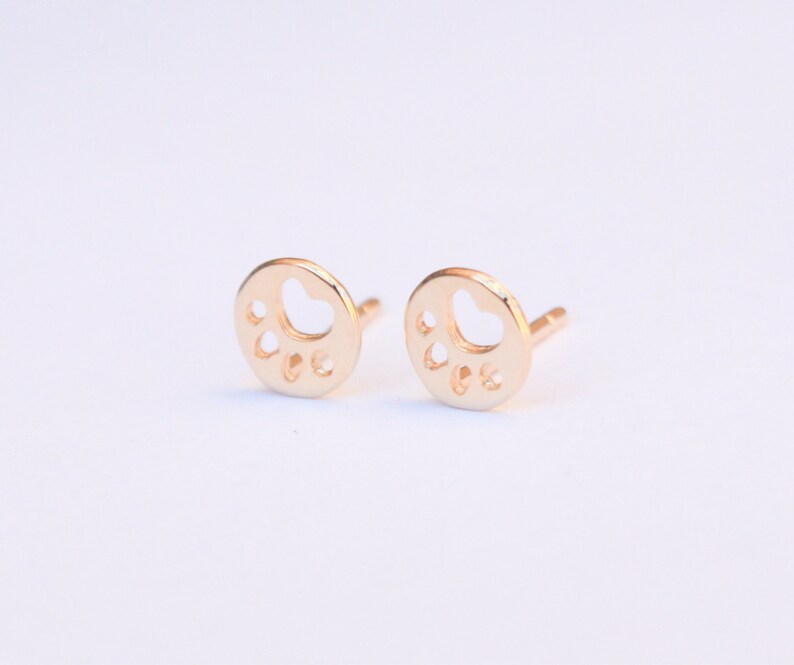 K&ouml;nnte beinhalten: Ein Paar goldfarbene Ohrstecker mit einem Pfotenabdruck-Design. Die Ohrringe sind klein und zart und w&auml;ren ein tolles Geschenk f&uuml;r einen Hundeliebhaber.
